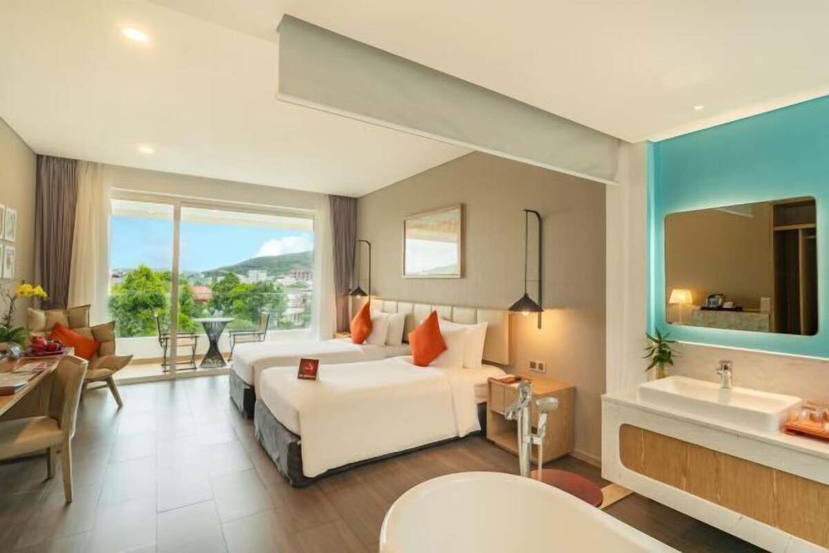 A hotel room with a large bed, a separate bathroom, a dining area, and a view of the outdoors.