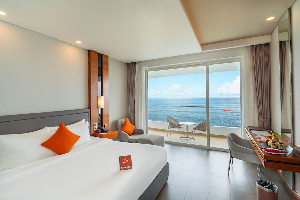 A hotel room with a bed, a desk with a view, and a balcony overlooking the sea.
