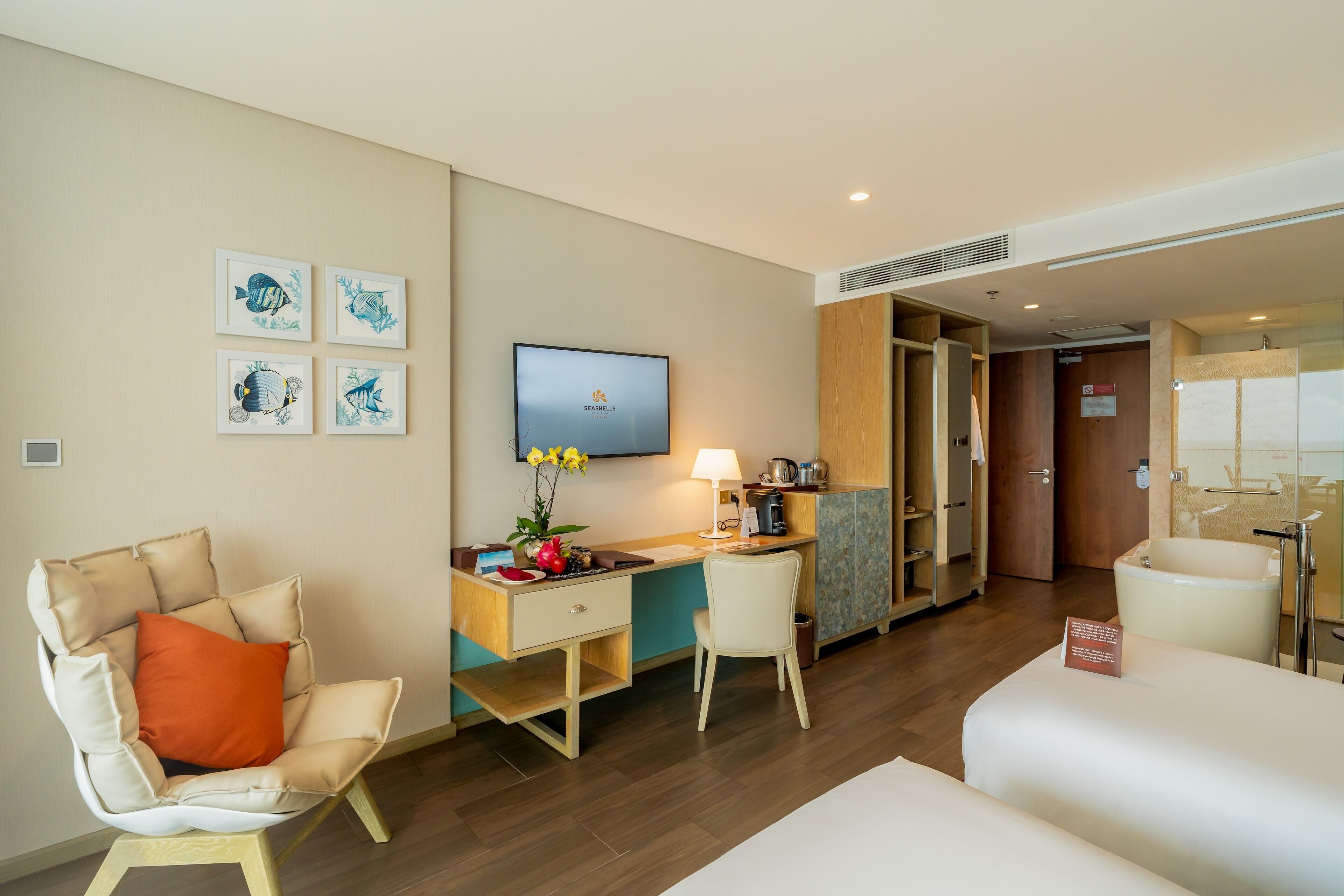 Habitación de hotel con cama, escritorio con computadora, una silla, televisor y cuadros en la pared.