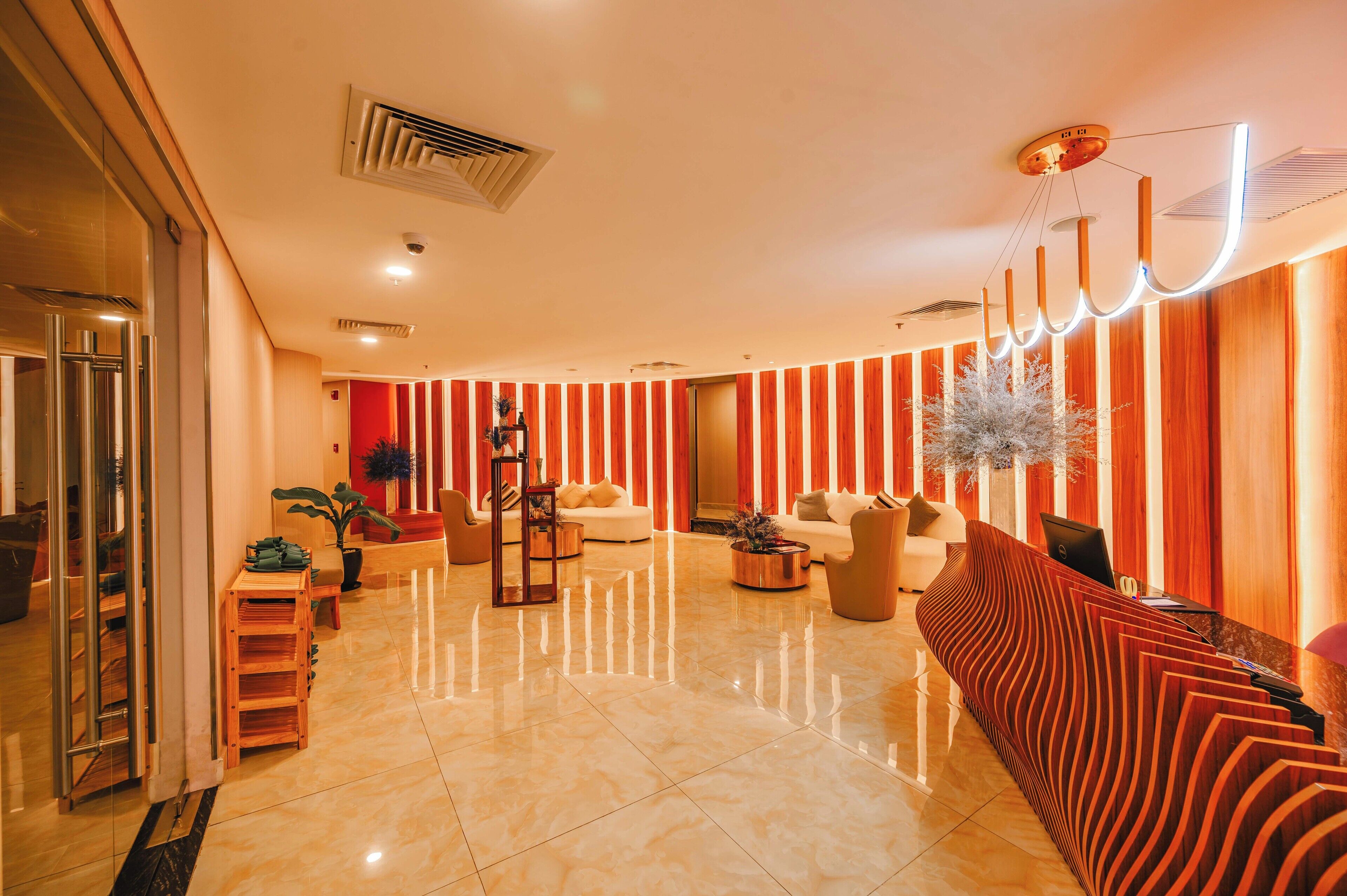 A spacious lobby with a modern reception desk, seating area, and a large potted plant.
