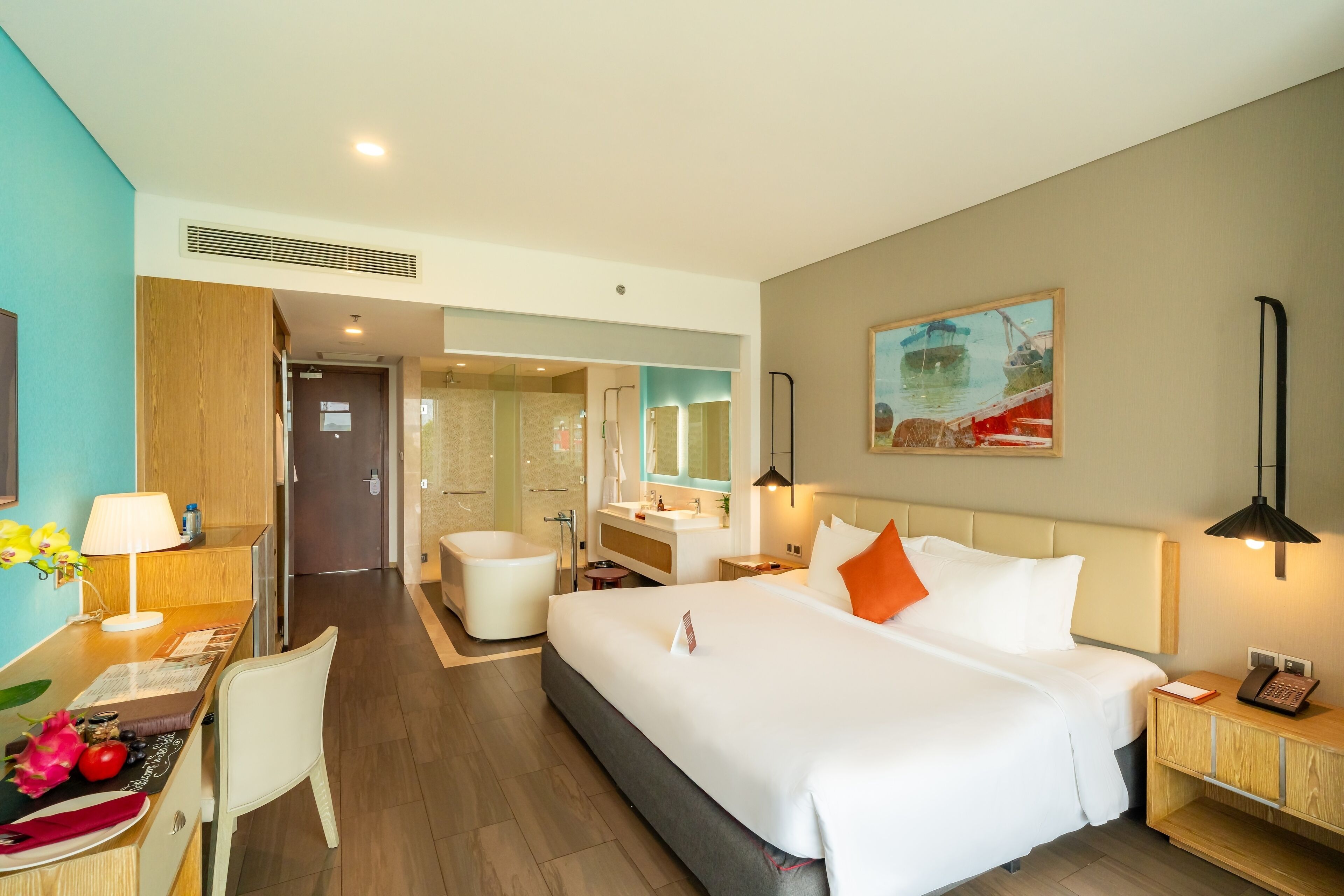A hotel room with a large bed, bedside table, lamp, and a desk with a chair.