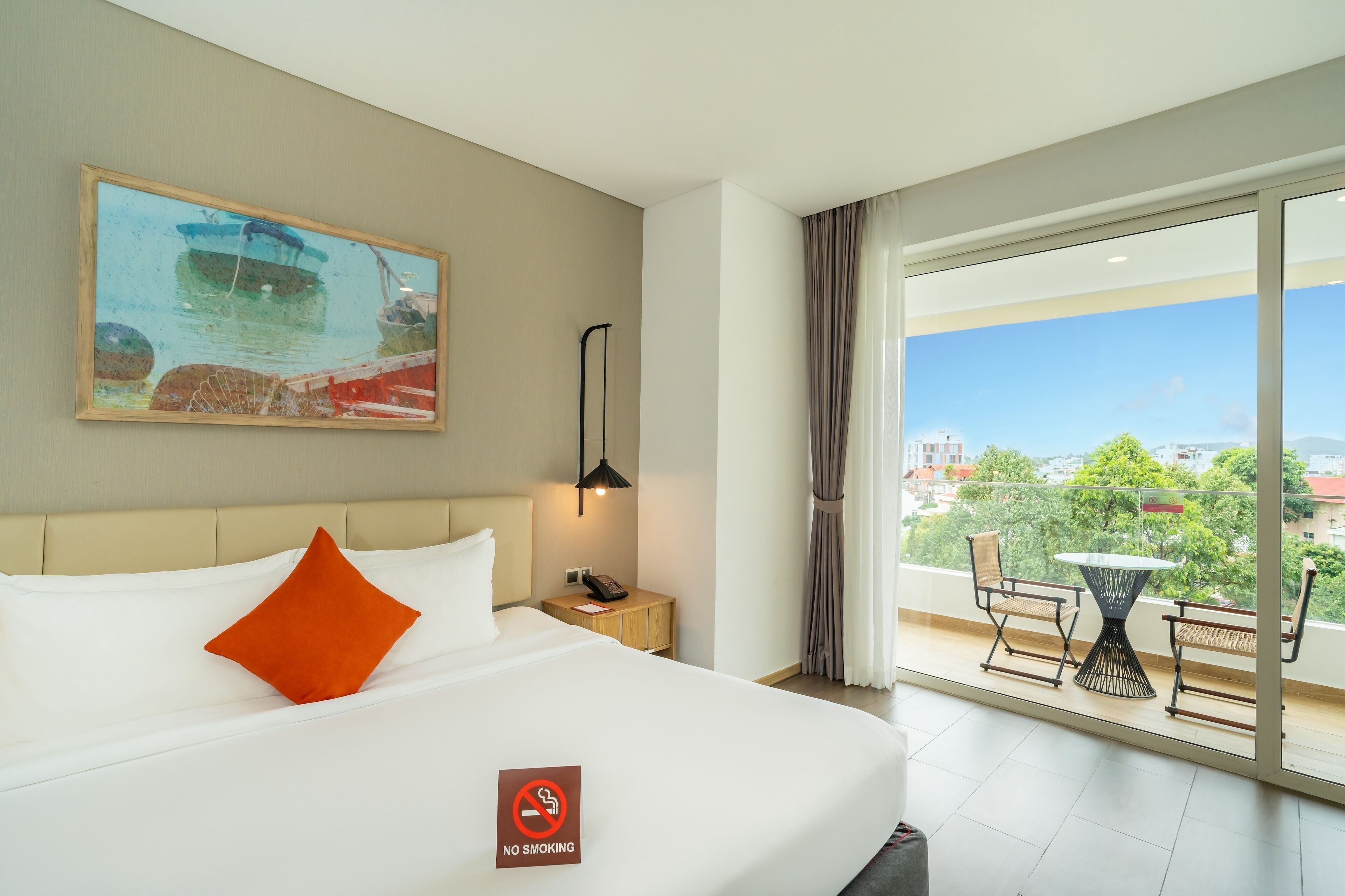 Hotelkamer met een bed, een schilderij, een nachtkastje, een tafel met stoelen en een balkon met uitzicht.