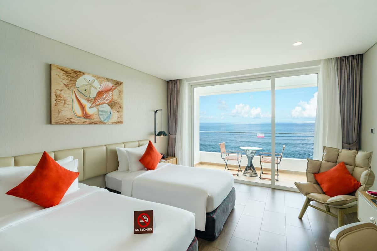 A hotel room with two beds, a painting on the wall, a view of the sea, and a balcony with a table and chairs.