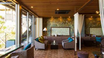 A modern lounge area with patterned sofas, a stone accent wall, and a glass railing overlooking a garden.