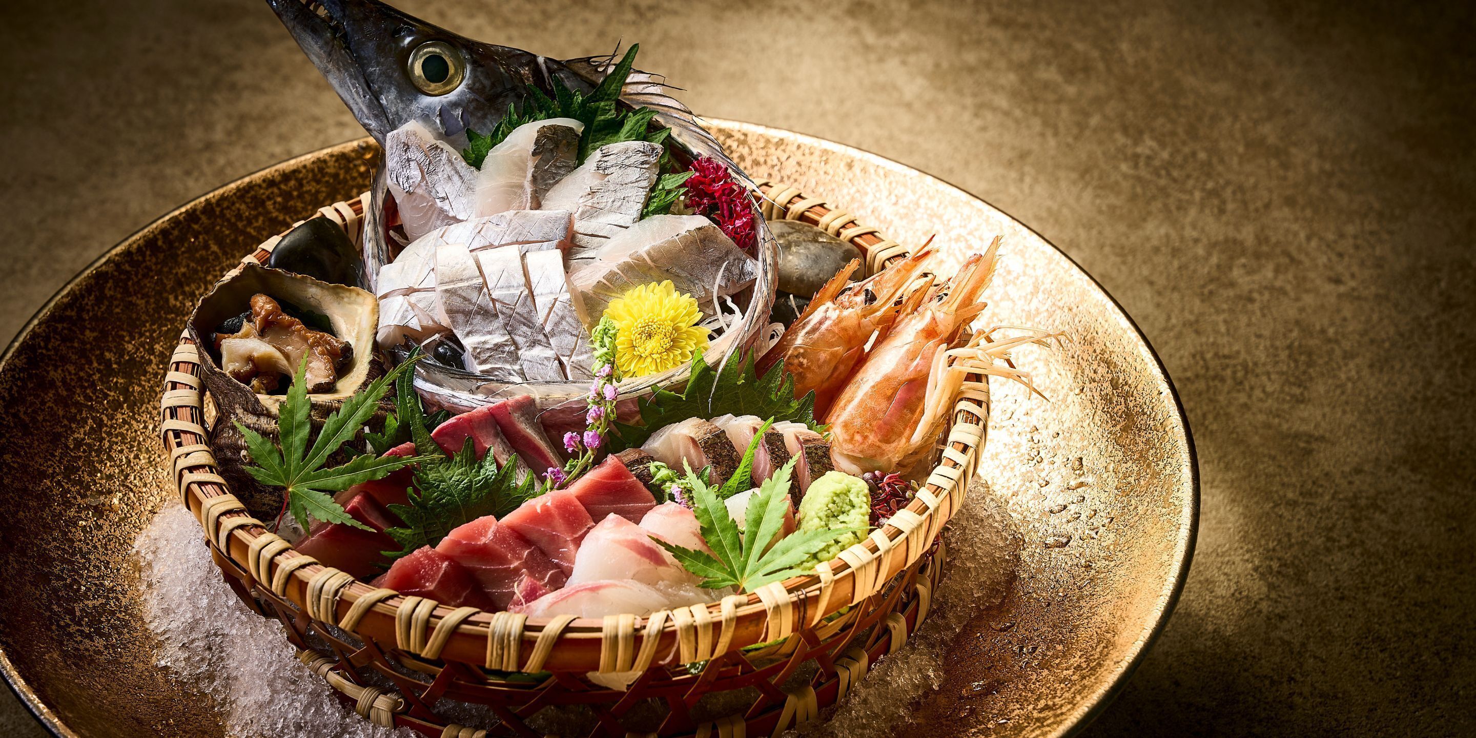 Una bandeja de mariscos con distintos tipos de pescado, camarones y adornos sobre un plato dorado.