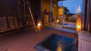 Una terraza de madera con un jacuzzi, un ventanal de vidrio que da a un dormitorio y un farol en el suelo.