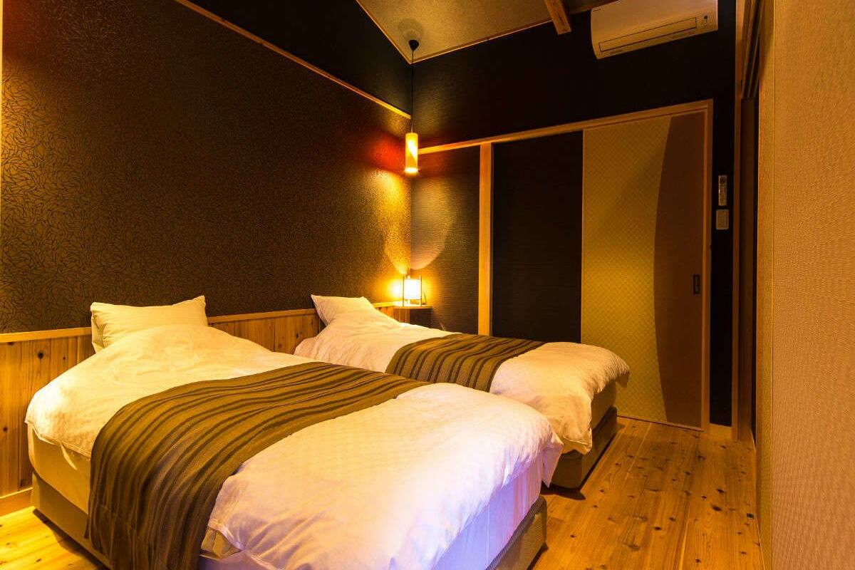 Una habitación con dos camas, suelo de madera y aire acondicionado de pared.