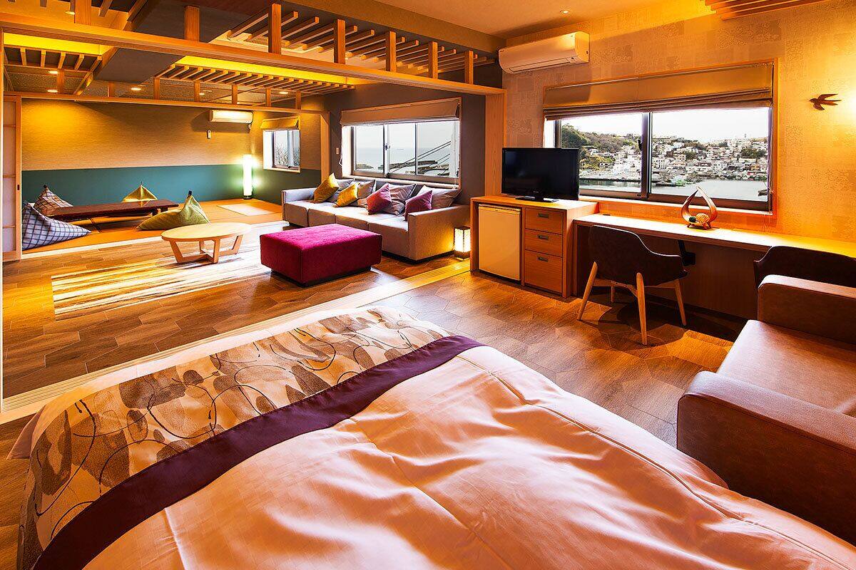 Habitación de hotel moderna con una cama grande, un escritorio, un televisor y vistas a un paisaje urbano.