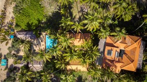An aerial view of a resort with multiple buildings, including a pool area, surrounded by palm trees. - Seven Turtles Resort (Rekawa)