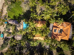 An aerial view of a resort with multiple buildings, including a pool area, surrounded by palm trees.