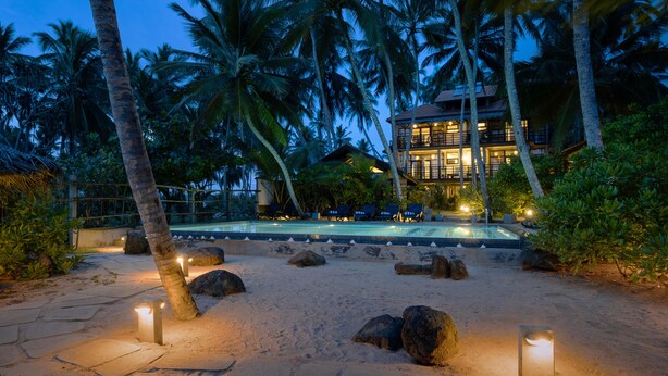 A resort with a pool, palm trees, and a well-lit building. - Seven Turtles Resort (Rekawa)