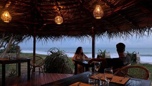 An outdoor dining area with a view of the ocean, wooden furniture, and hanging lights. - Seven Turtles Resort (Rekawa)