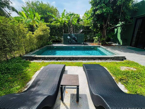 A rectangular swimming pool with a tiled border, surrounded by lush greenery and a grassy area with two black lounge chairs and a small table. - Seava House Ao-Nang Krabi (Krabi)