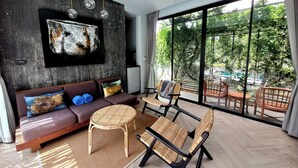 Een moderne woonkamer met een bank, stoelen, een ronde tafel en een groot raam met uitzicht op groen.