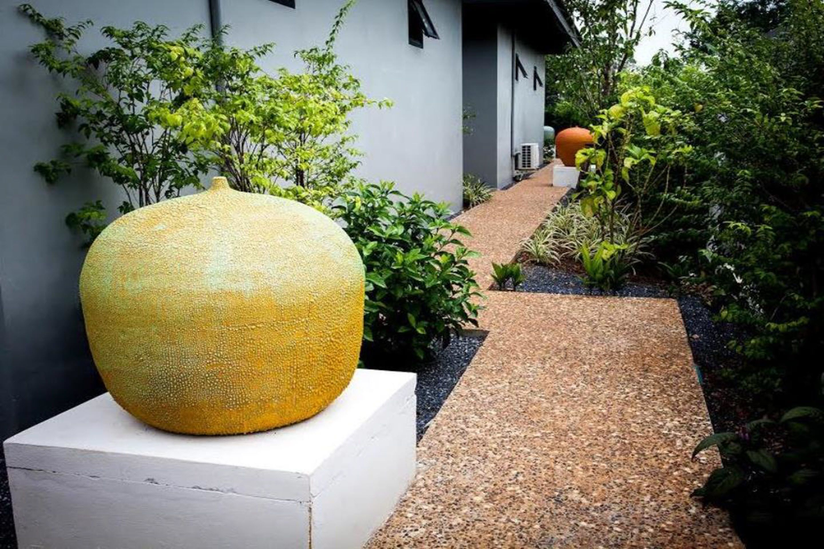 Een tuinpad dat leidt naar een gebouw met een grote gele sculptuur op een voetstuk.