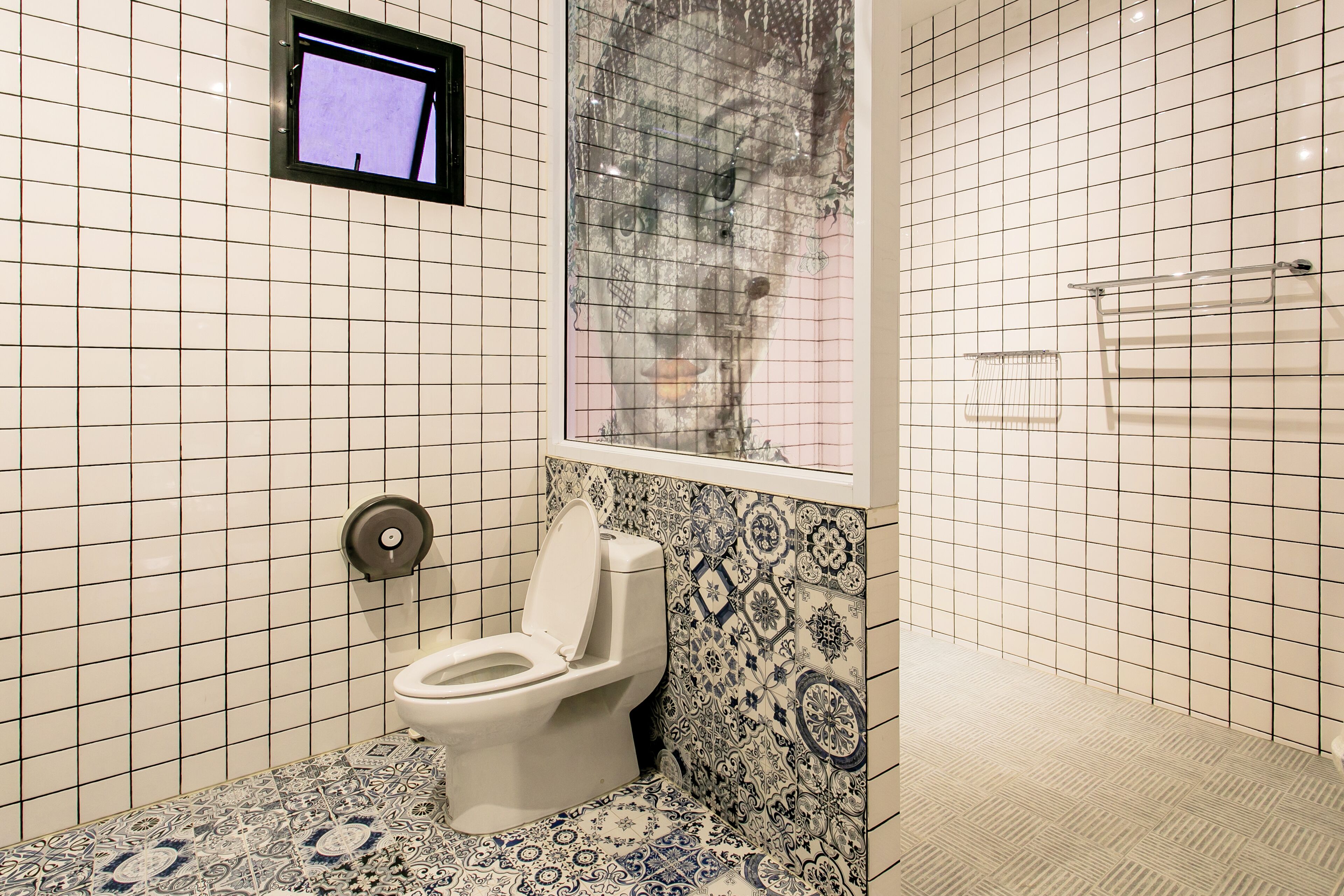 Un baño con inodoro, ventana y baldosas estampadas.