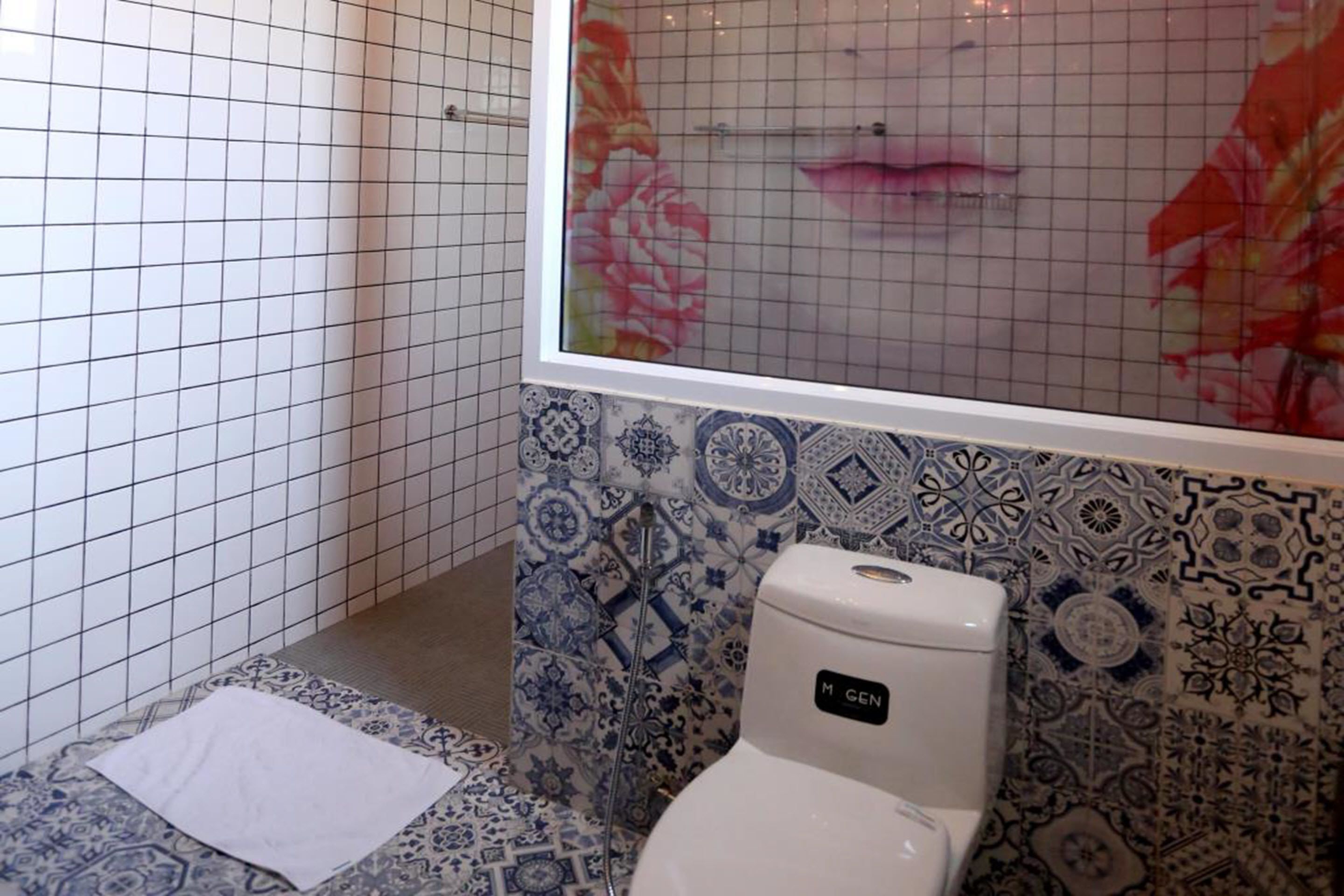 Een badkamer met toilet, douche en een betegelde muur met bloemendesign.