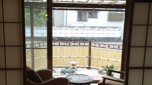 A traditional Japanese room with tatami flooring, a low table, two chairs, and a view of a bamboo fence and a building outside. - Guest house Enishi - Hostel (Toyama)
