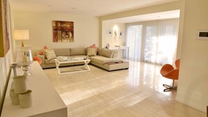 A modern living room with a sofa, coffee table, and a dining area with a chair. - Villa Roma on Capri - GC (Surfers Paradise)