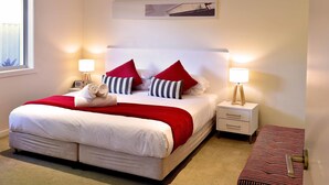 A neatly made bed with red and white bedding, two bedside lamps, a small bedside table, and a wall-mounted picture. - Villa Roma on Capri - GC (Surfers Paradise)