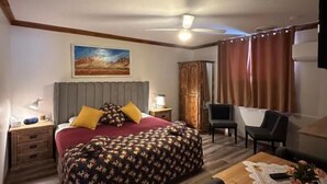 Een hotelkamer met een bed, een bureau, een stoel, een plafondventilator en een schilderij aan de muur.