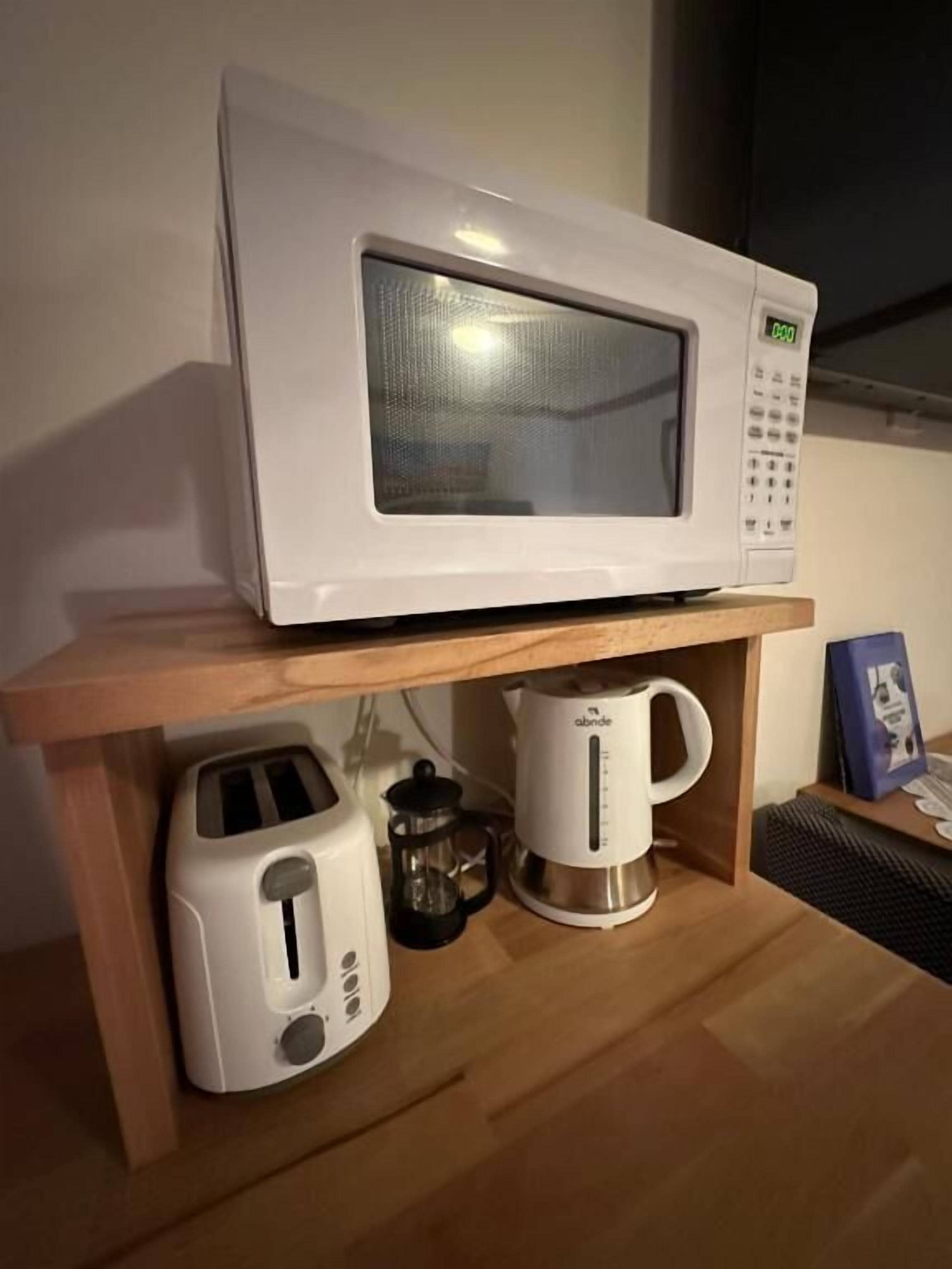 A microwave on a wooden shelf, a toaster, and a coffee maker.