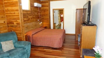 A room with wooden walls, a bed with a checkered blanket, a blue sofa, a wooden cabinet, and a television.