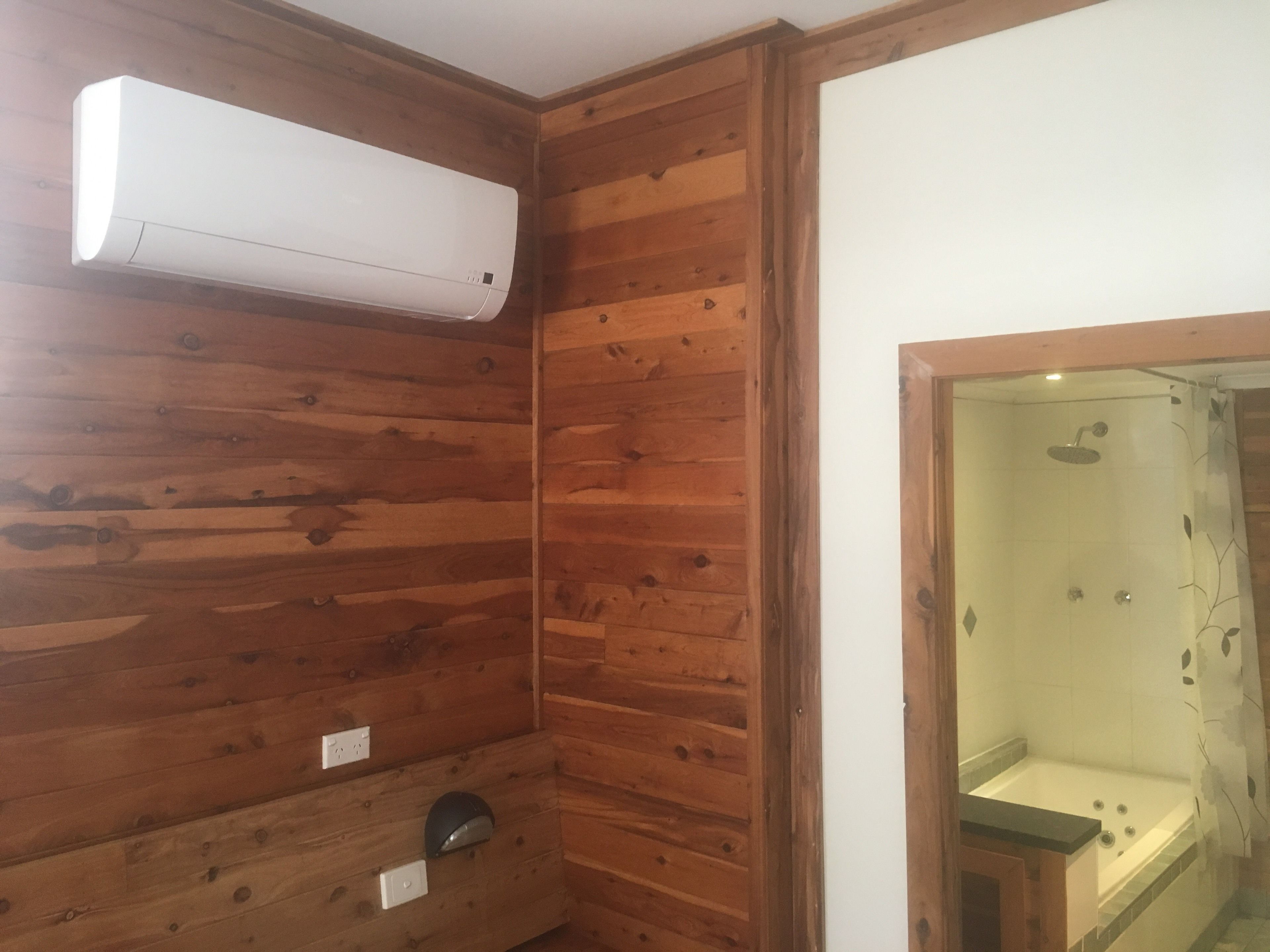 Ein Zimmer mit Holzvertäfelung, einer eingebauten Klimaanlage, einem Duschbereich mit Glastür und einem kleinen Waschbecken.