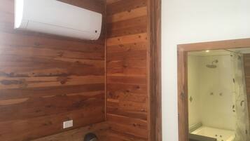 Ein Zimmer mit Holzvertäfelung, einer eingebauten Klimaanlage, einem Duschbereich mit Glastür und einem kleinen Waschbecken.