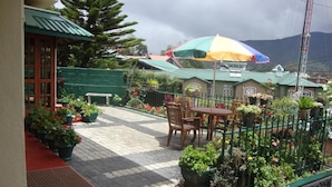 Un espace patio aménagé avec une table et des chaises, entouré de plantes en pot et agrémenté d’un parasol aux couleurs vives.