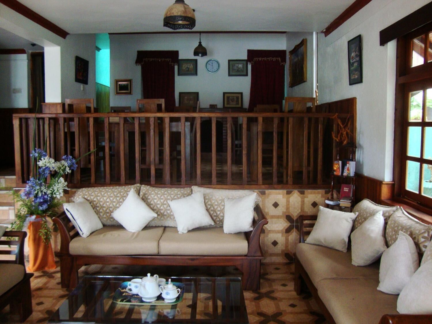 A cozy living room with a sofa set, a coffee table with tea set, and a decorative vase with flowers.
