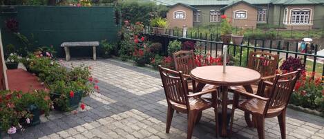 Un patio con una mesa y sillas de madera redondas, rodeado de macetas con plantas y flores.