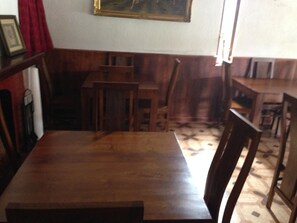 A room with a wooden table and chairs, a red curtain, and a painting on the wall. - Richmond Inn (Nuwara Eliya)