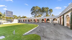 A motel with a 24-hour check-in service, outdoor parking, and a covered walkway with arches.