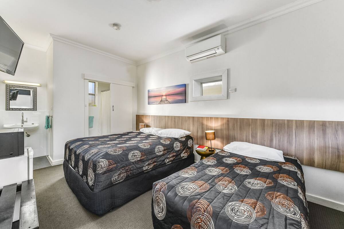 A hotel room with two beds, a desk, a sink, and a mirror.