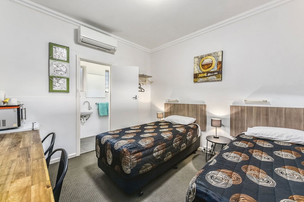 A hotel room with two beds, a desk, a chair, a sink, and an air conditioning unit.