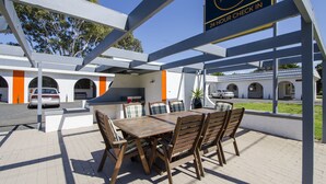 An outdoor seating area with a wooden table and chairs, a sign for Rest Motels, and a view of the hotel building in the background.