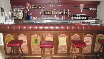 A bar area with a checkered floor, a counter with bottles and glasses, and stools with labels.