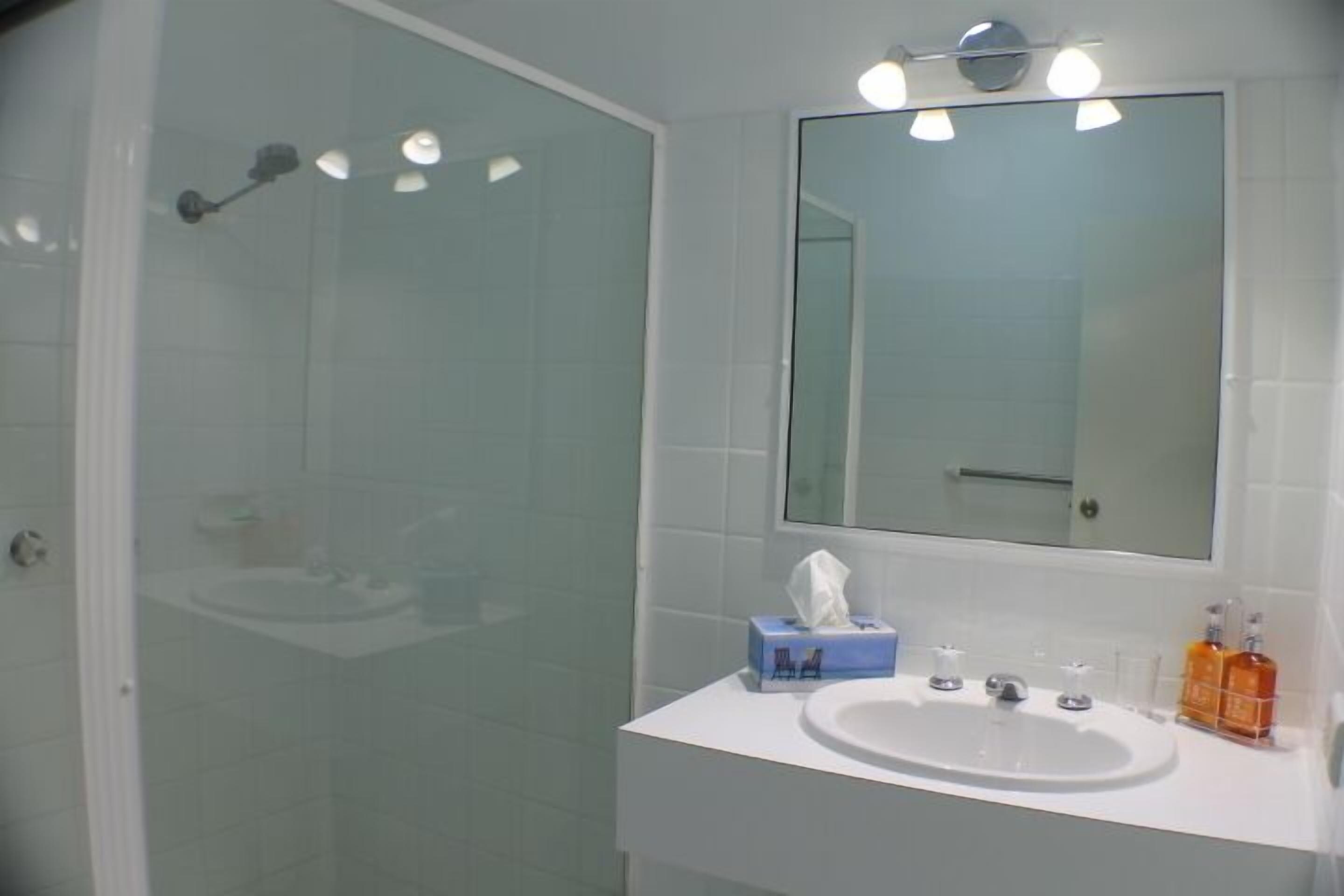 A bathroom with a glass shower enclosure, a white sink, a mirror, and a towel dispenser.