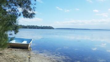 A calm lake with a small boat on the shore, surrounded by trees and a clear sky.