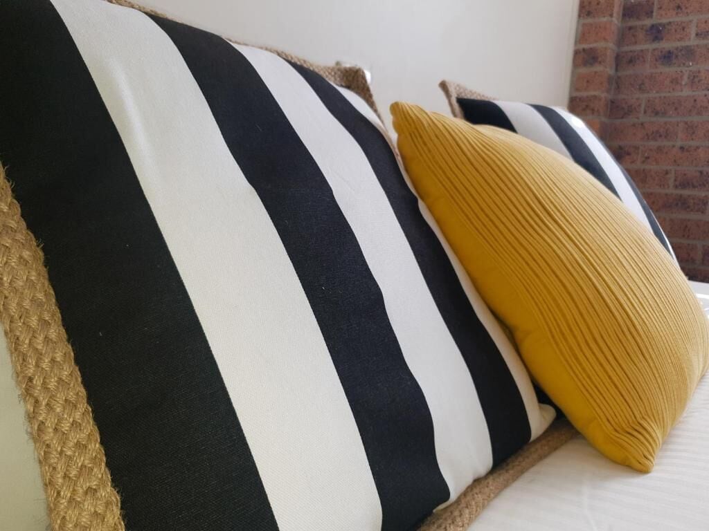 A bed with striped bedding and a single yellow pillow.