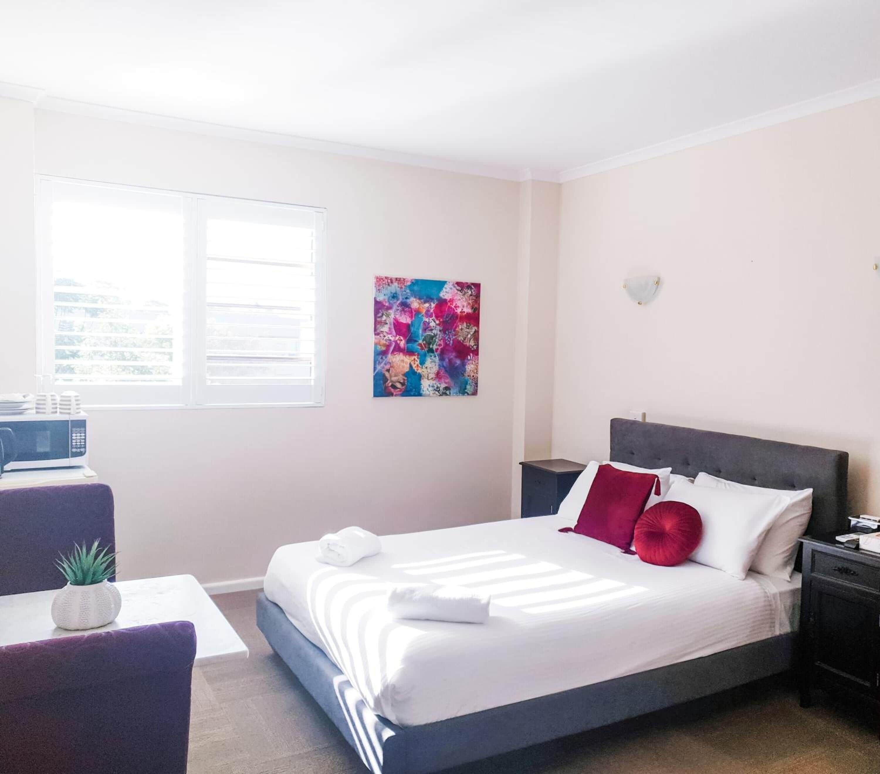 A neatly arranged hotel room with a bed, a desk, and a window.