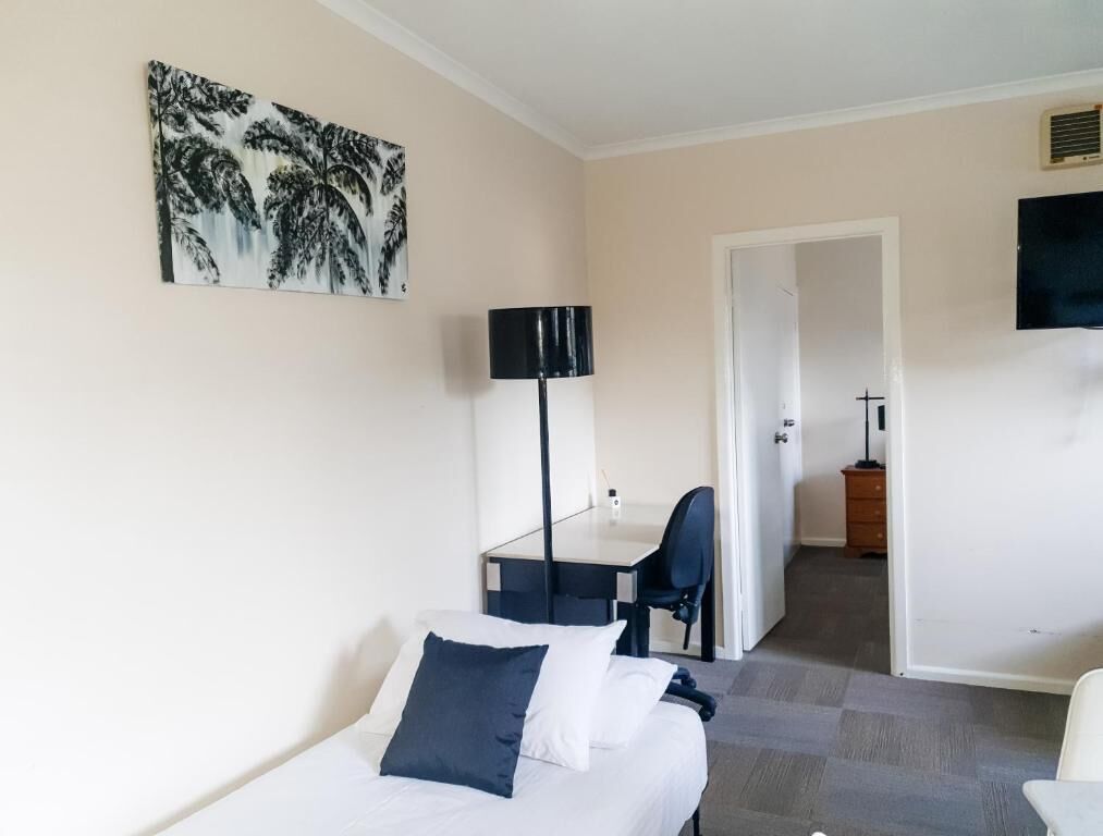 A hotel room with a bed, a desk, a chair, and a painting on the wall.
