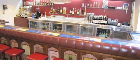 A bar area with a counter, stools, and various bottles and glasses.