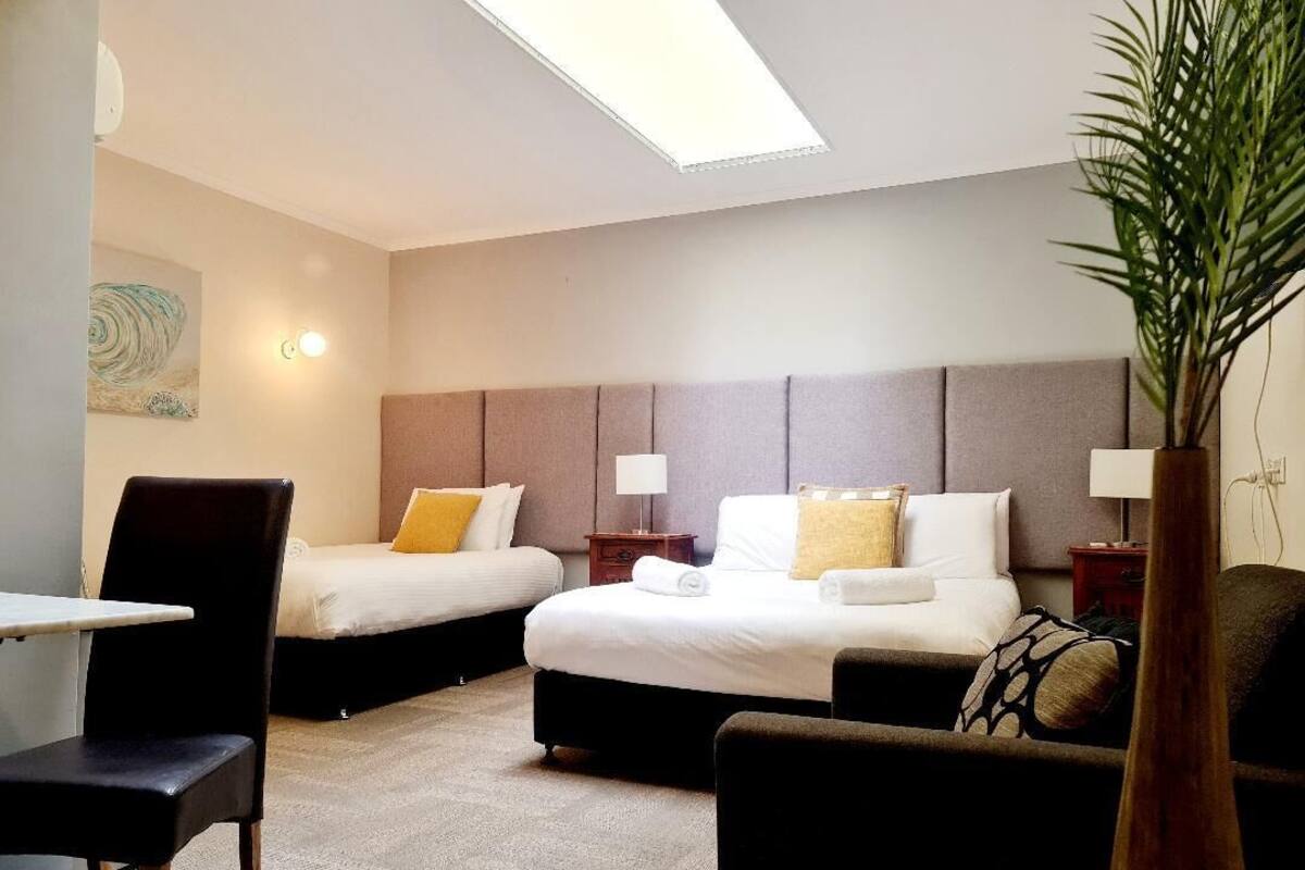 Habitación de hotel con dos camas, un escritorio, una silla y una planta.