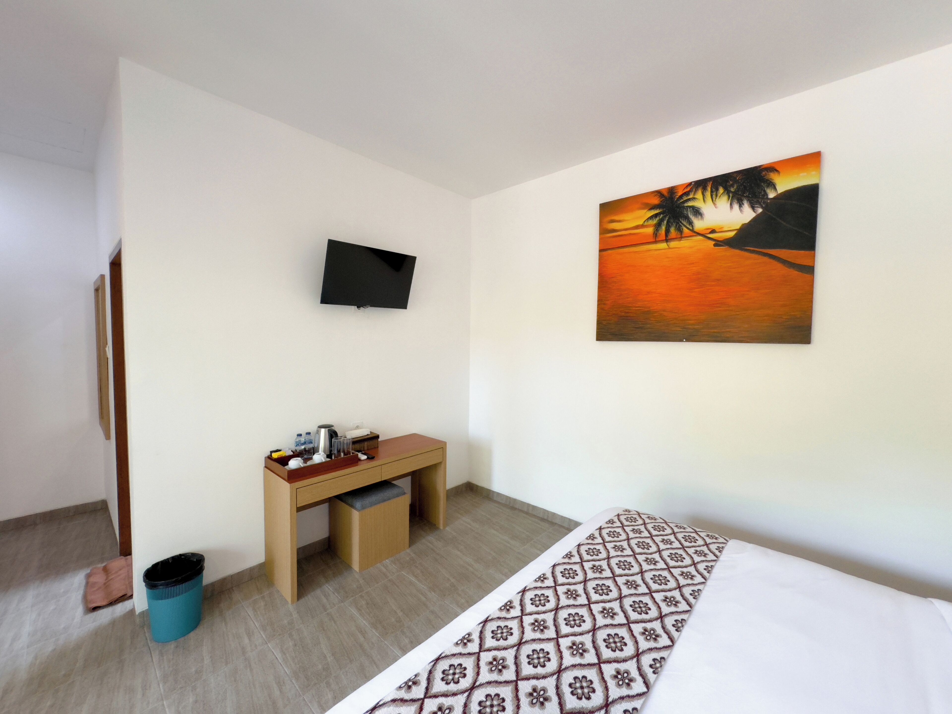 Une chambre d’hôtel avec un lit, un bureau, une chaise, une poubelle, un téléviseur et un tableau au mur.
