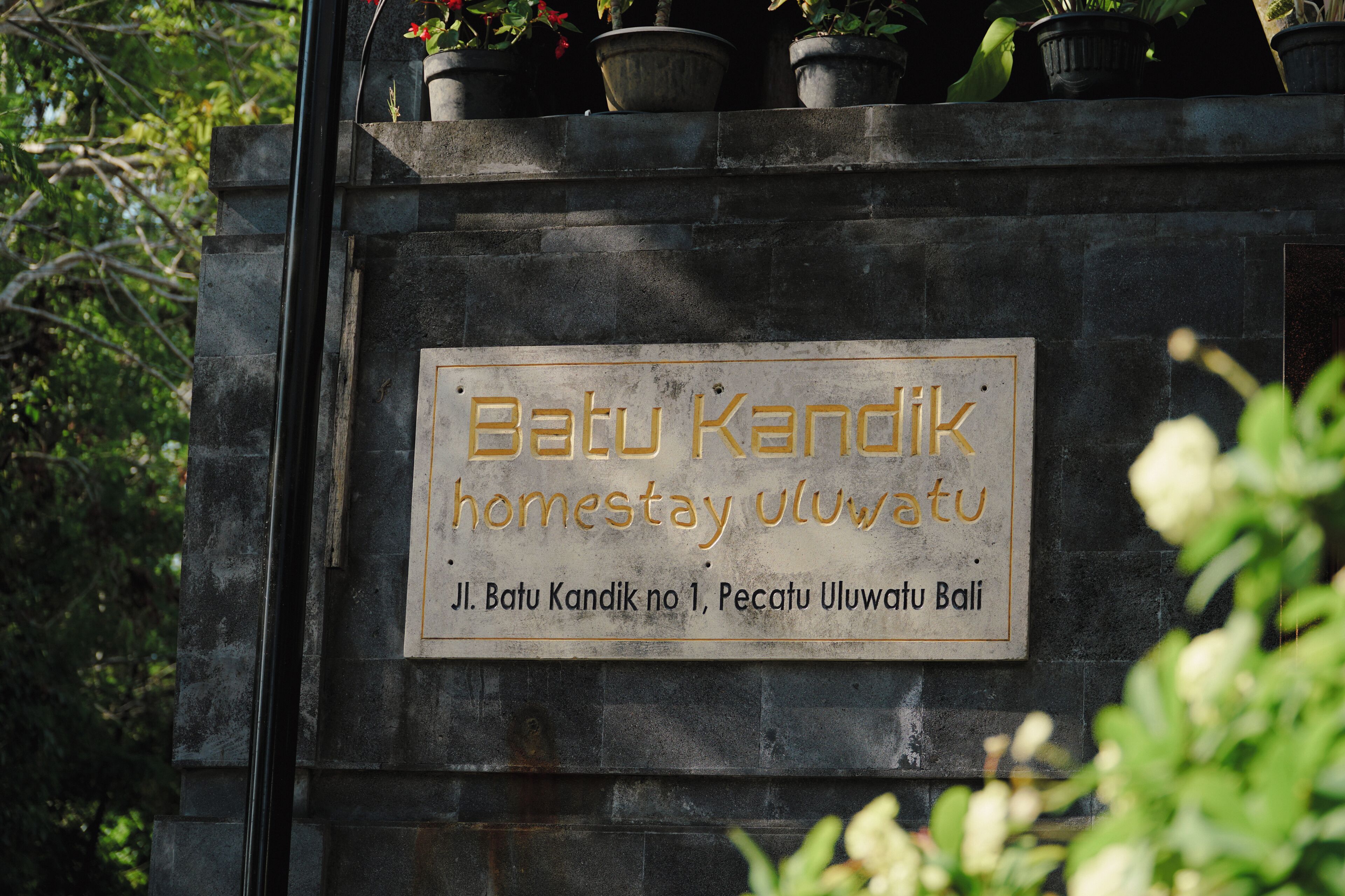 A stone plaque with text indicating a location named "Batu Kandik homestay uluwatu" and a reference to "Jl. Batu Kandik no 1, Pecatu Uluwatu Bali."