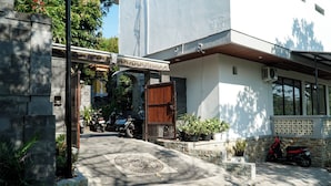A modern building with a concrete entrance, a wooden door, and a paved driveway. - Batu Kandik Homestay (Pecatu)