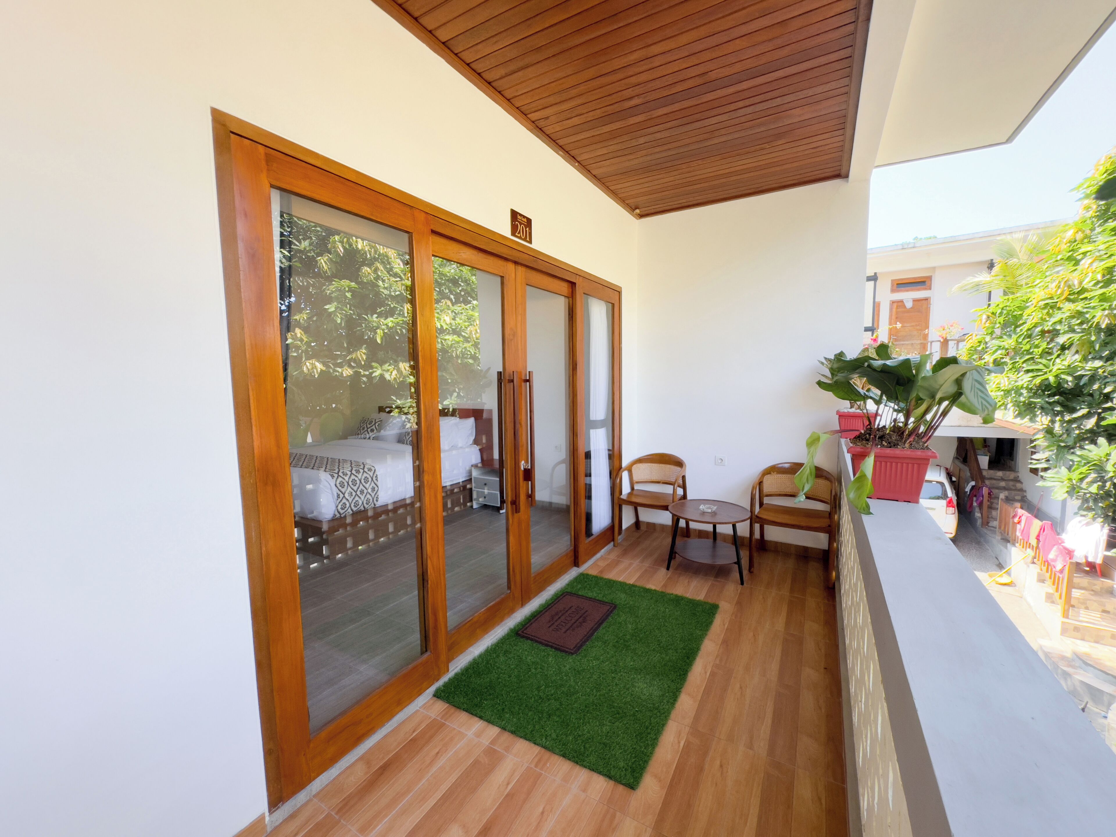 A balcony with a wooden floor, a bed with patterned bedding, and two chairs.