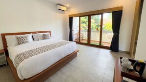 A hotel room with a large bed, a sliding glass door to a balcony, a desk with a kettle, and an air conditioning unit on the wall. - Batu Kandik Homestay (Pecatu)